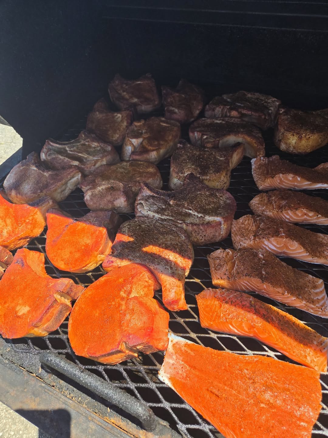 Pork chops and salmon fillets smoking side by side on the smoker